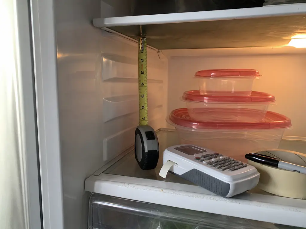 Tape measure held vertically inside a refrigerator to check clearance between a shelf and the one above it