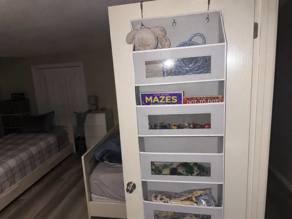 Over the door organizer loaded with toys on a rental bedroom door in a shared small kids room