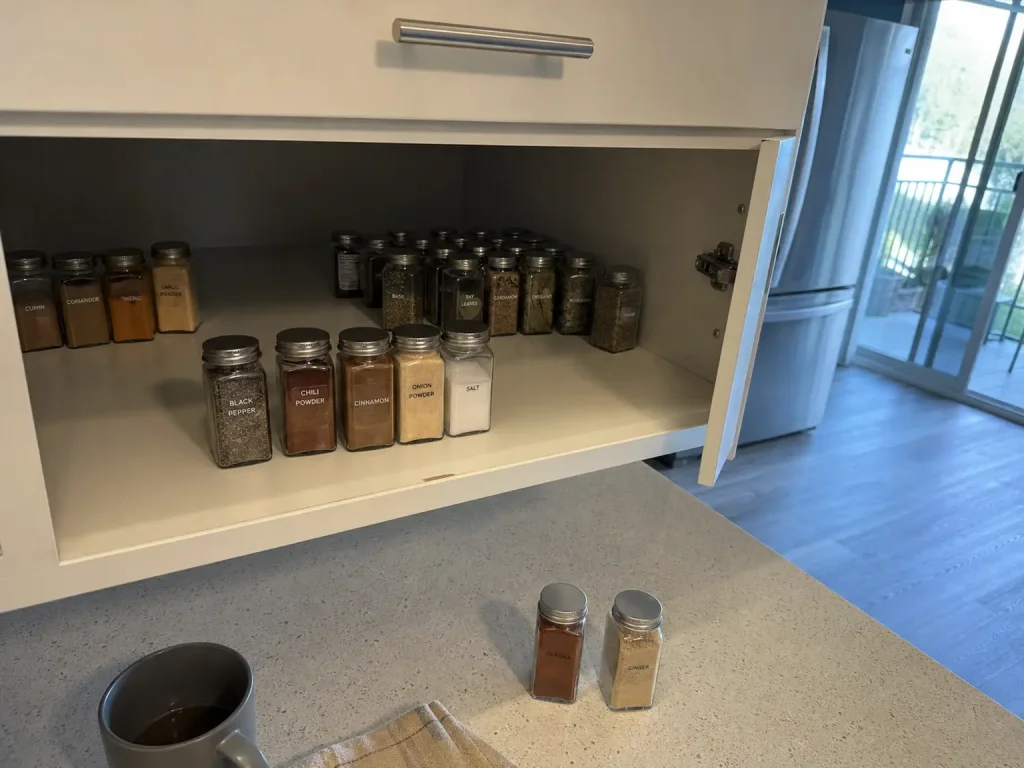 Spice jars grouped on an open cabinet shelf with the everyday ones pulled to the front row