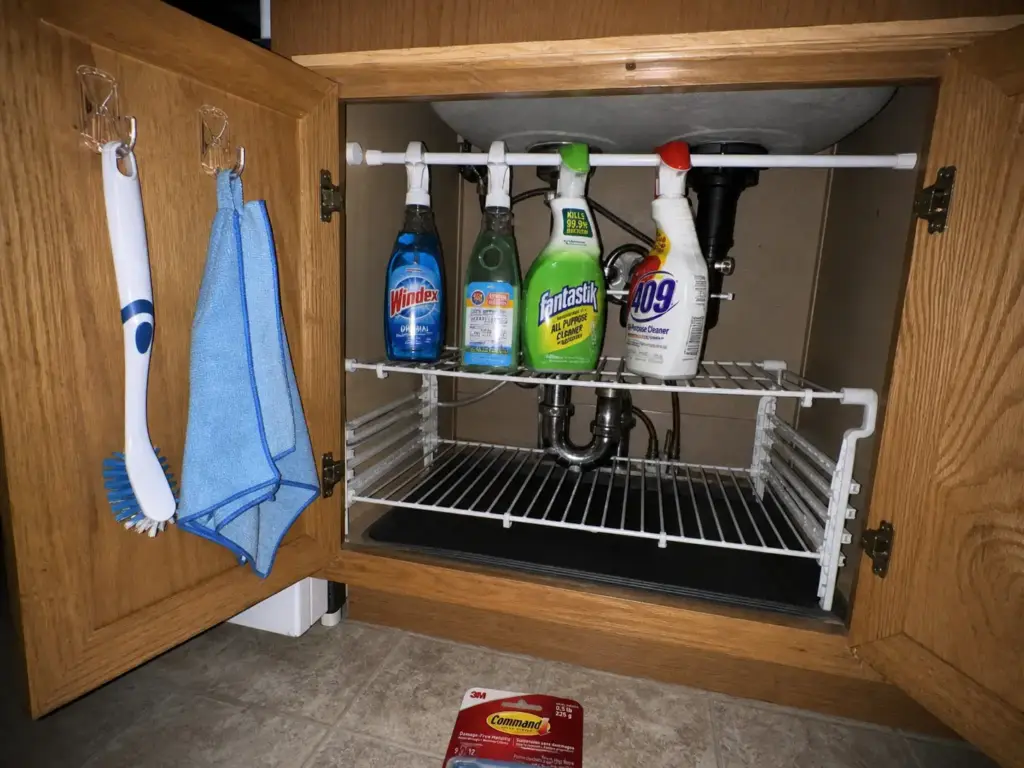 Spray bottles hanging from a tension rod and door hooks above the P-trap in an under sink cabinet