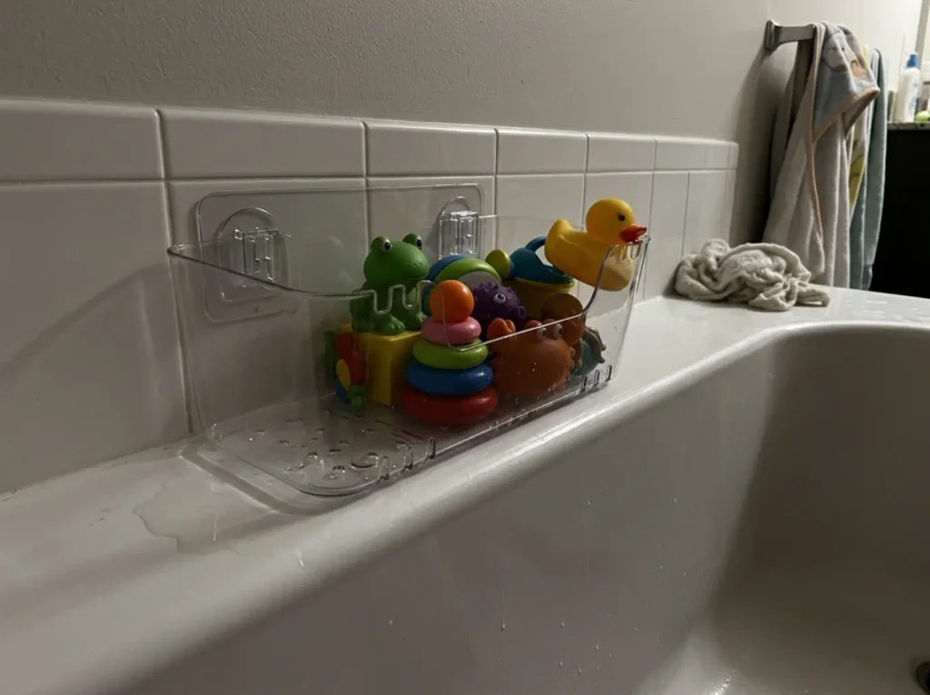 Bath toy organizer with drain holes holding toys on the tub wall of a rental bathroom