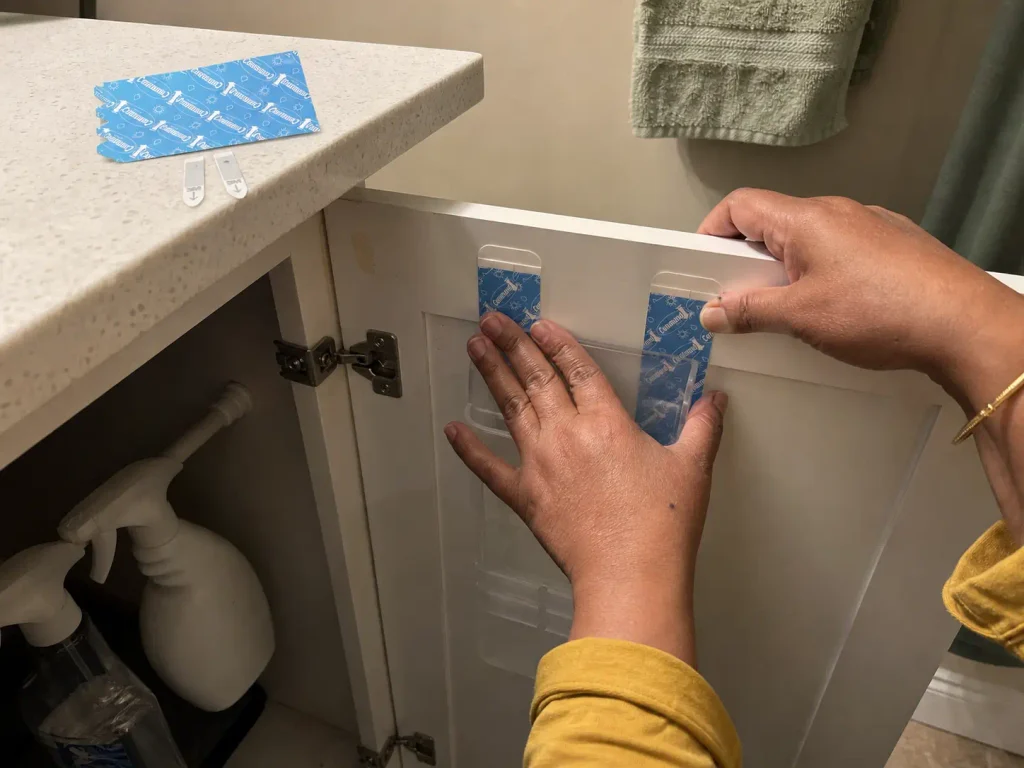 Hands pressing a water-resistant adhesive strip onto the inside of a bathroom cabinet door