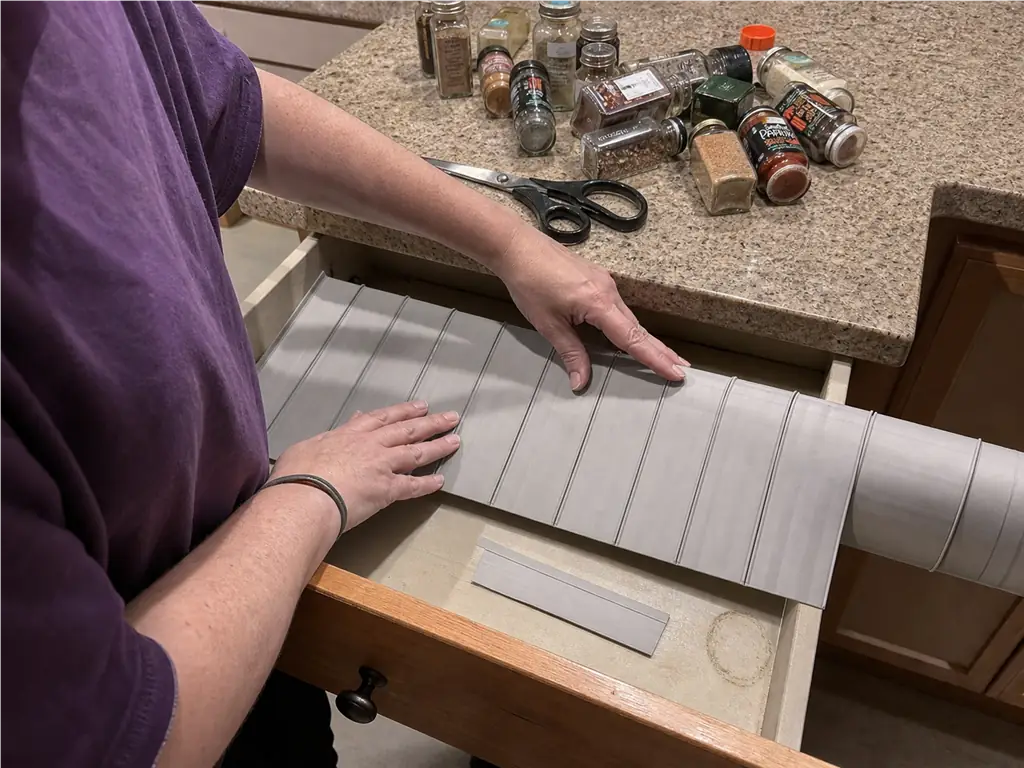 Spice Drawer vs Spice Rack? Your Tape Measure Decides 8 Hands trimming a non-slip spice drawer liner to size to stop jars from rolling in the drawer