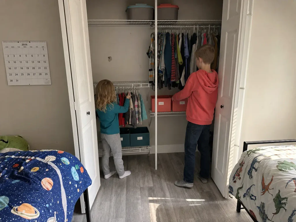 Narrow shared kids closet split into two color-coded zones for siblings