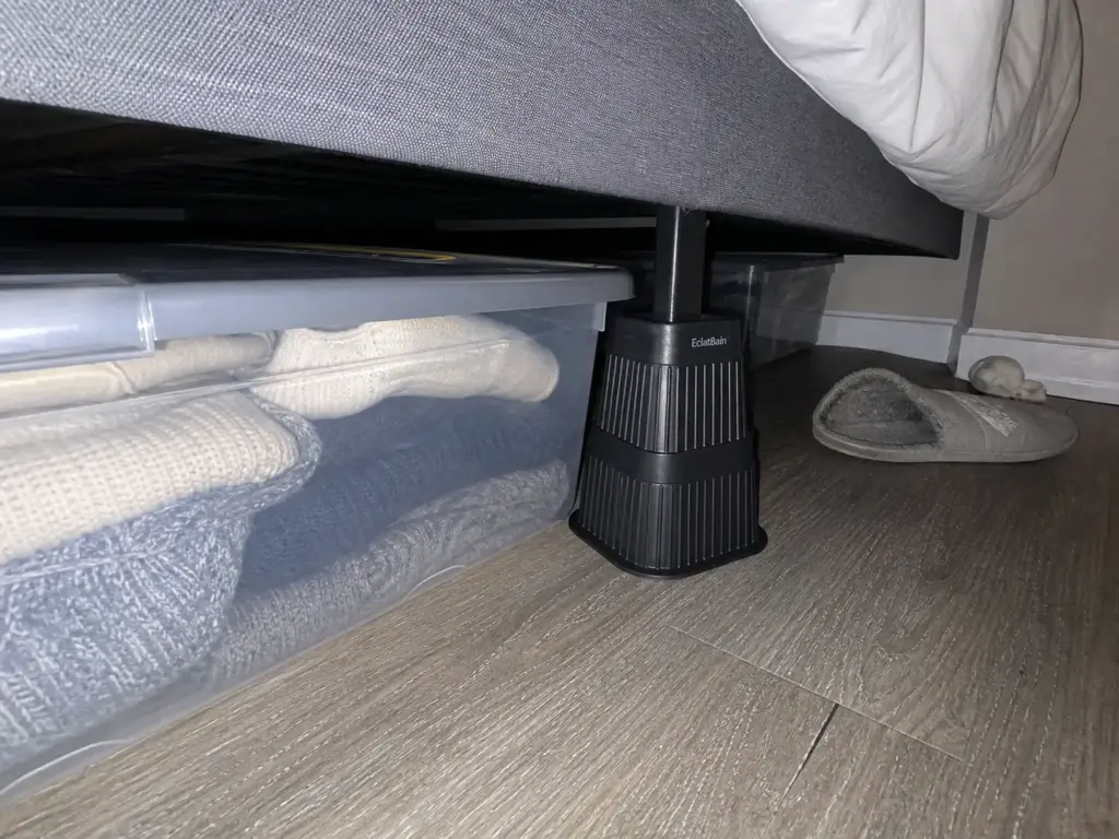 Bed risers lifting a bed frame to create under-bed storage clearance for flat bins