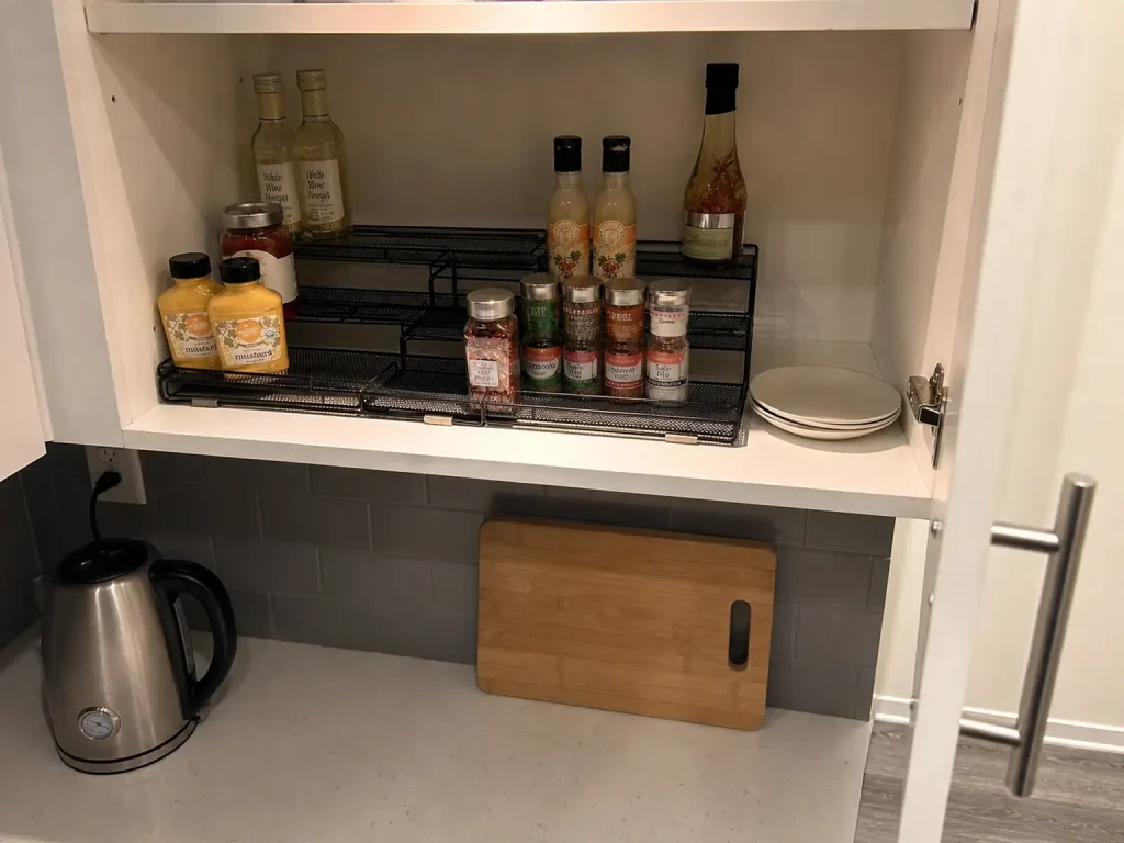 Three tier expandable spice rack organizer holding jars in stepped rows inside an open kitchen cabinet