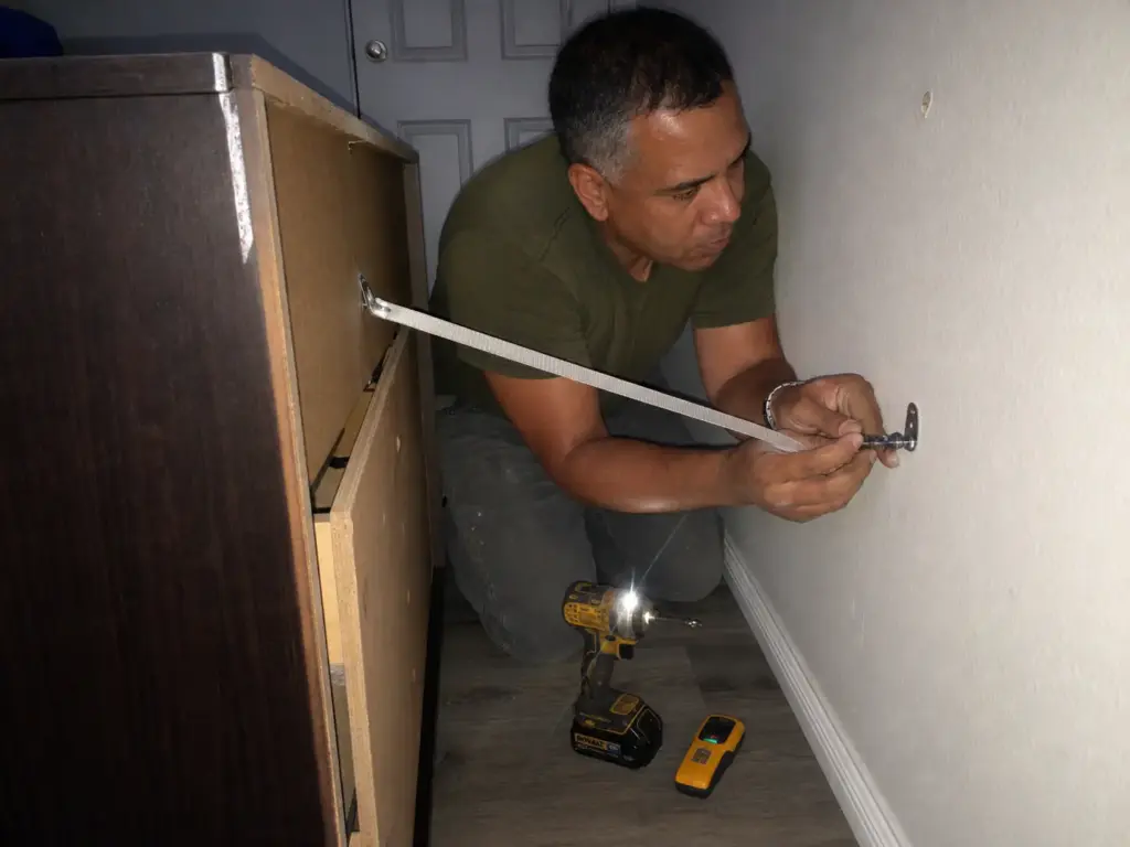 Anti tip strap being fastened from the back of a dresser to the bedroom wall