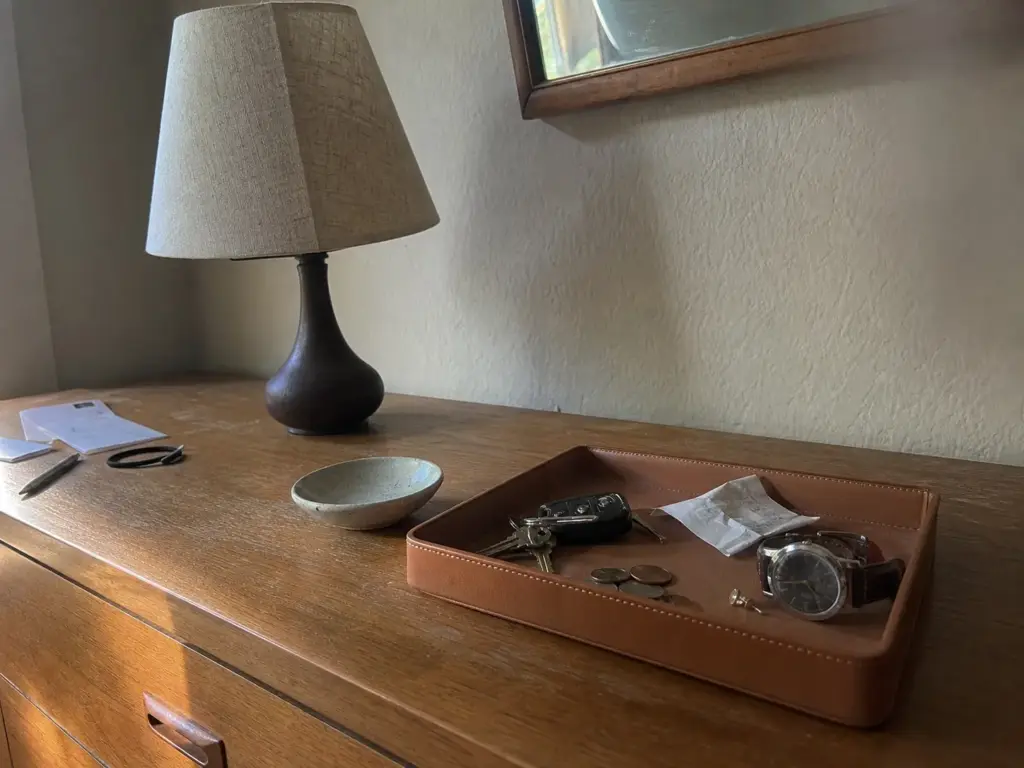 Dresser top with a catch-all tray holding keys, coins and a watch beside a lamp