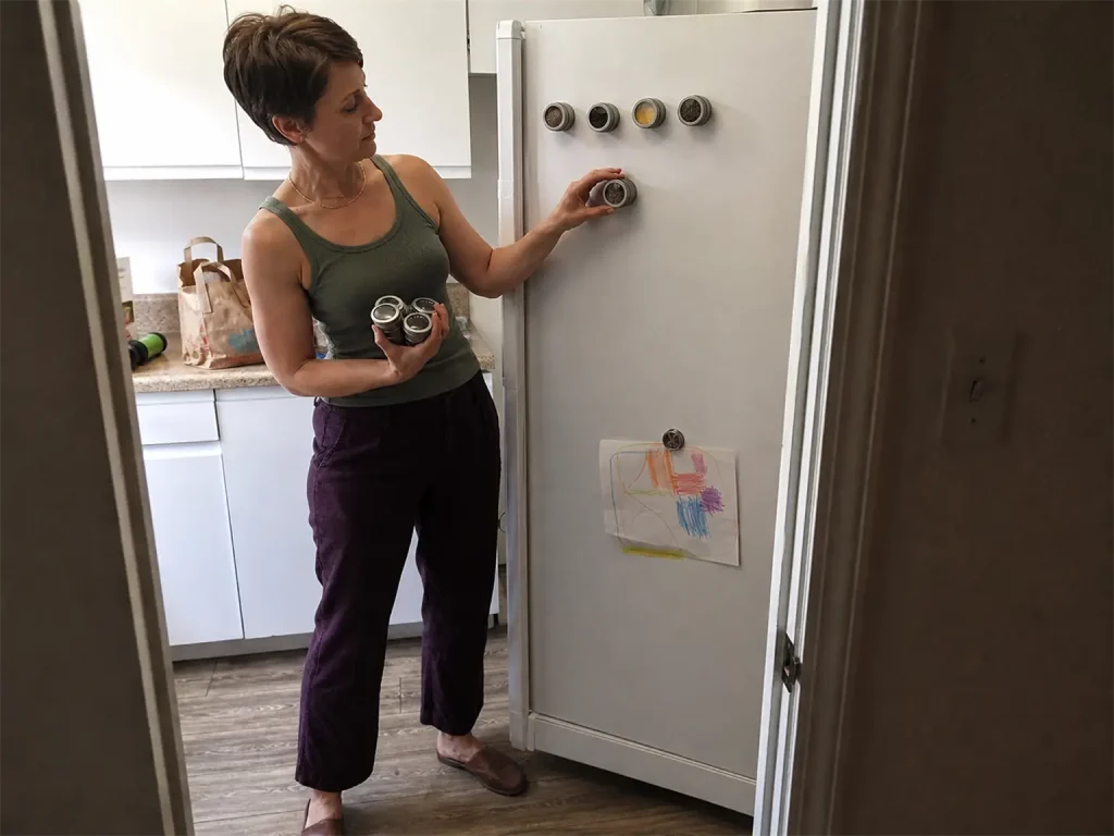 Best Spice Rack Organizers That Actually Stay Put 12 Woman testing a magnetic spice tin on a rental fridge door before mounting the set
