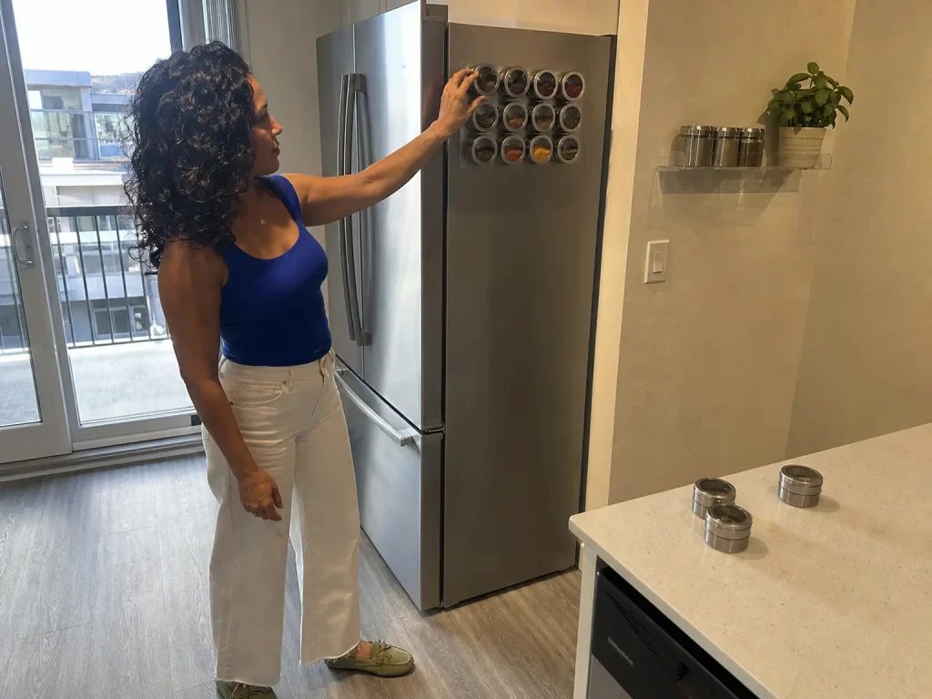 Woman placing a magnetic spice tin on the side of a fridge in a small rental kitchen with no drilling