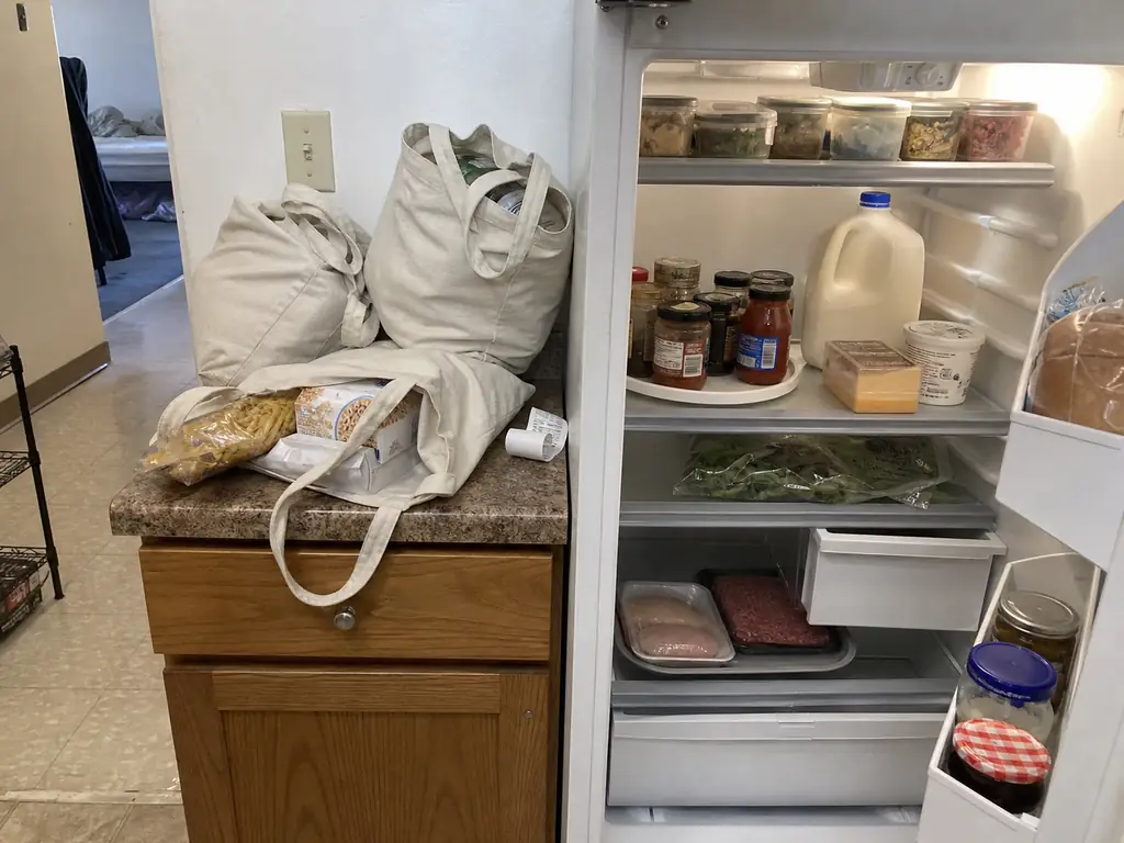 Grocery bags on a counter beside an open refrigerator with cold items being loaded first
