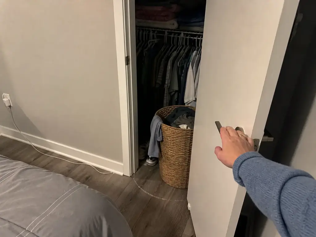 Closet door stopped partway open by a laundry hamper in a small bedroom walkway
