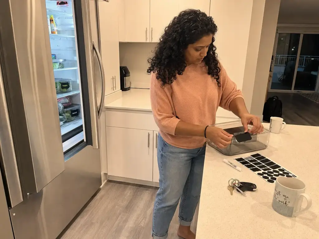 Woman labeling a clear bin with a removable chalkboard label to mark her shelf in a shared fridge