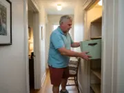 Best Linen Closet Organizers for 12-Inch Shelves Man loading fabric bins into a narrow hallway linen closet with shallow shelves in an older home