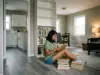 How to Organize a Bookshelf That Stays That Way Woman mid-project sorting books into piles on the floor beside a half-empty bookshelf