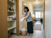 How to Fold Towels for a Linen Closet Without Collapse Woman folding a bath towel in thirds beside an open linen closet in a small starter home