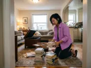 Out of Shelf Space? Organize Books in a Small Apartment Woman sorting book stacks on the living room floor of a small apartment with no bookshelf