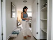Why Your Small Linen Closet Fills Up Again in Weeks Woman sorting towel stacks in front of a narrow hallway linen closet during a small linen closet organization reset