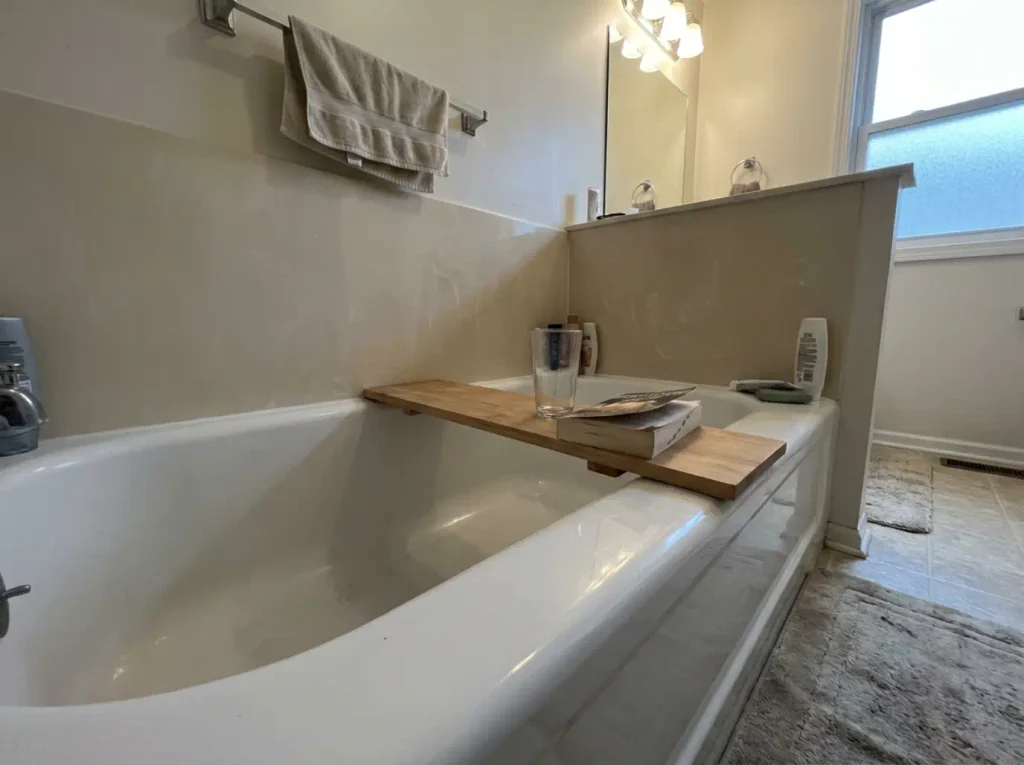 Bath tray resting crooked across a tub rim with one foot hanging over the basin edge