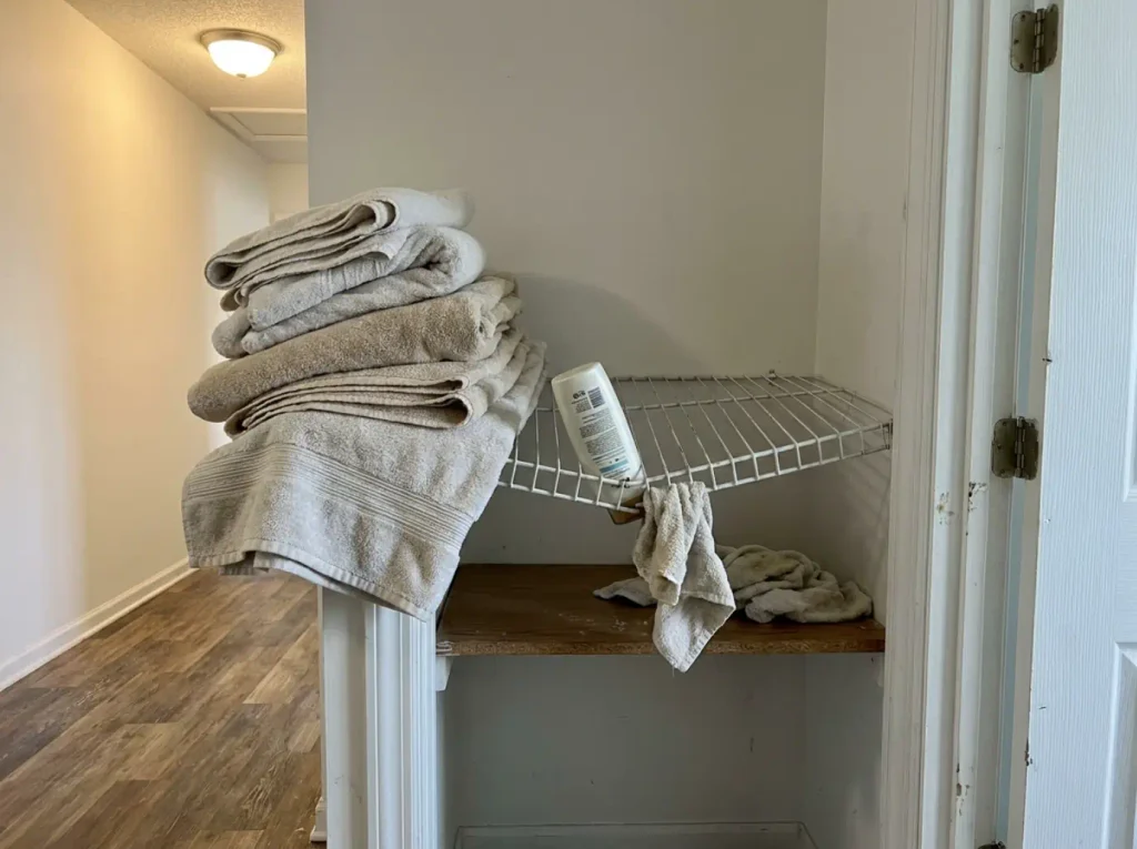 Leaning towel stack and a bottle tipped through the gaps of a wire linen closet shelf