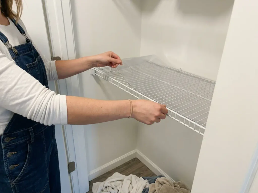 Hands laying a clear vinyl liner over a white wire linen closet shelf