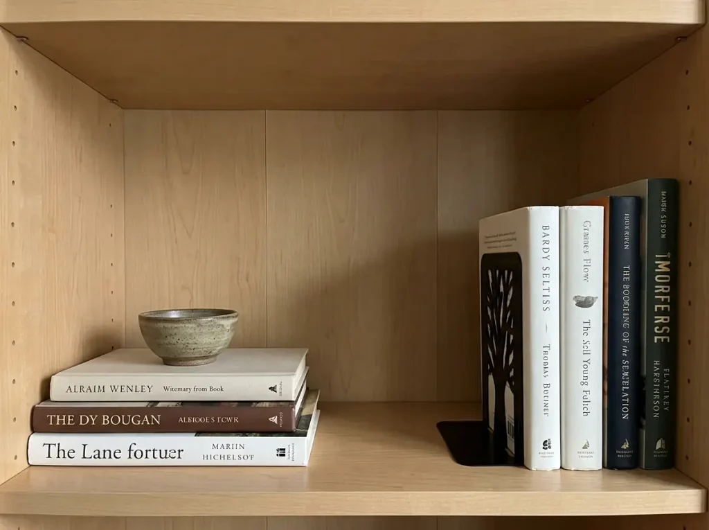 Bookshelf styling with a flat book stack topped by a bowl beside an upright run held by a metal tree bookend