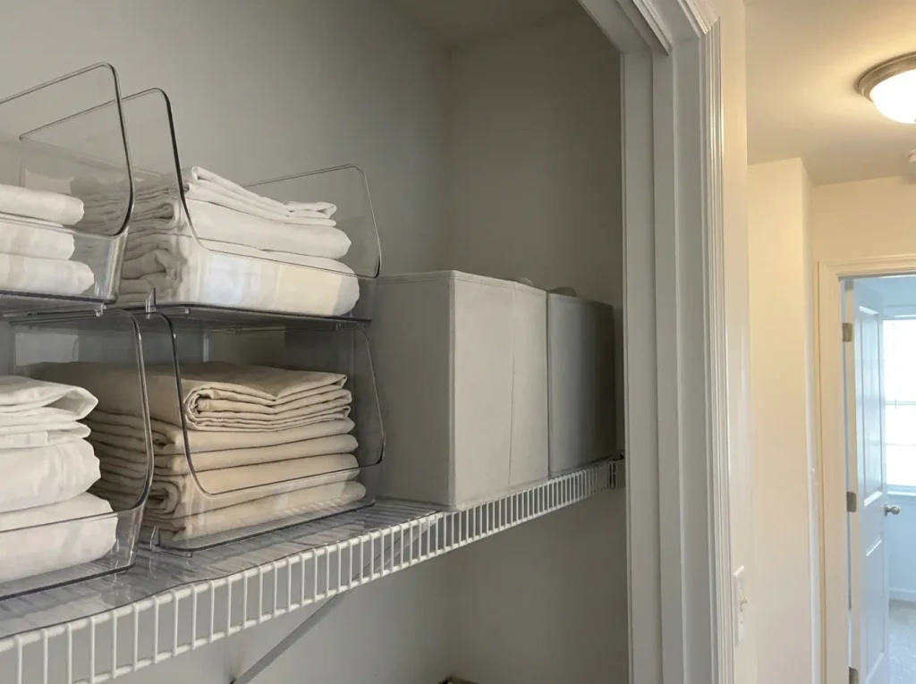 Clear stacking bins beside opaque fabric bins on a rental linen closet shelf