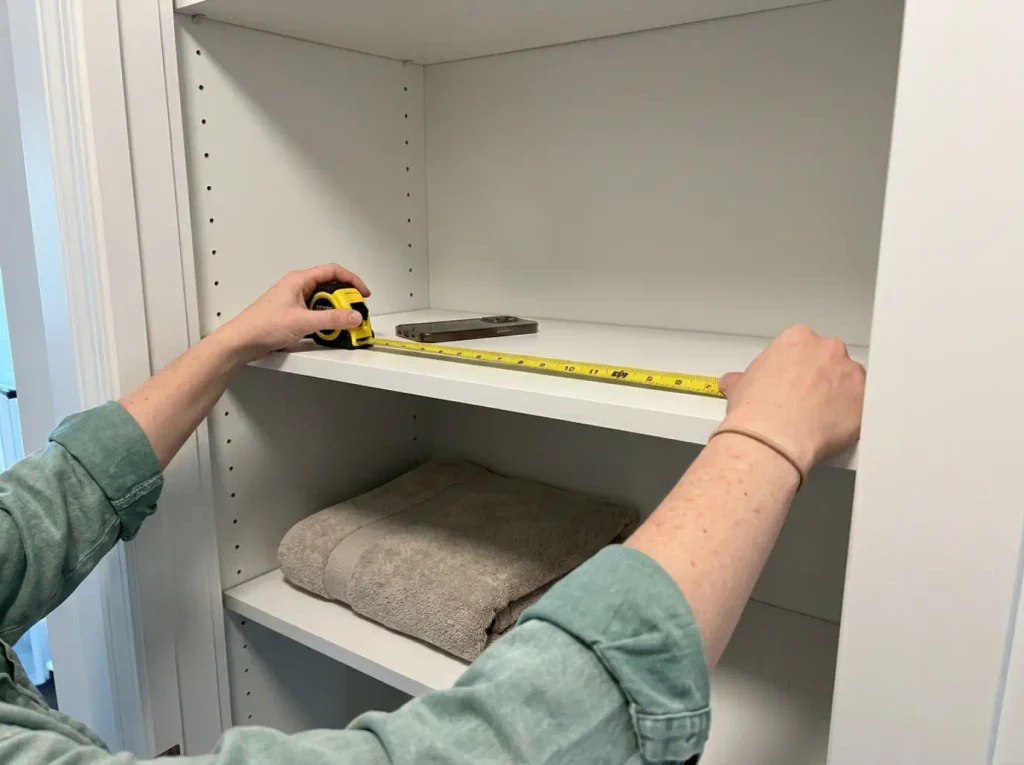 Hands measuring the depth of an empty linen closet shelf with a retractable tape measure