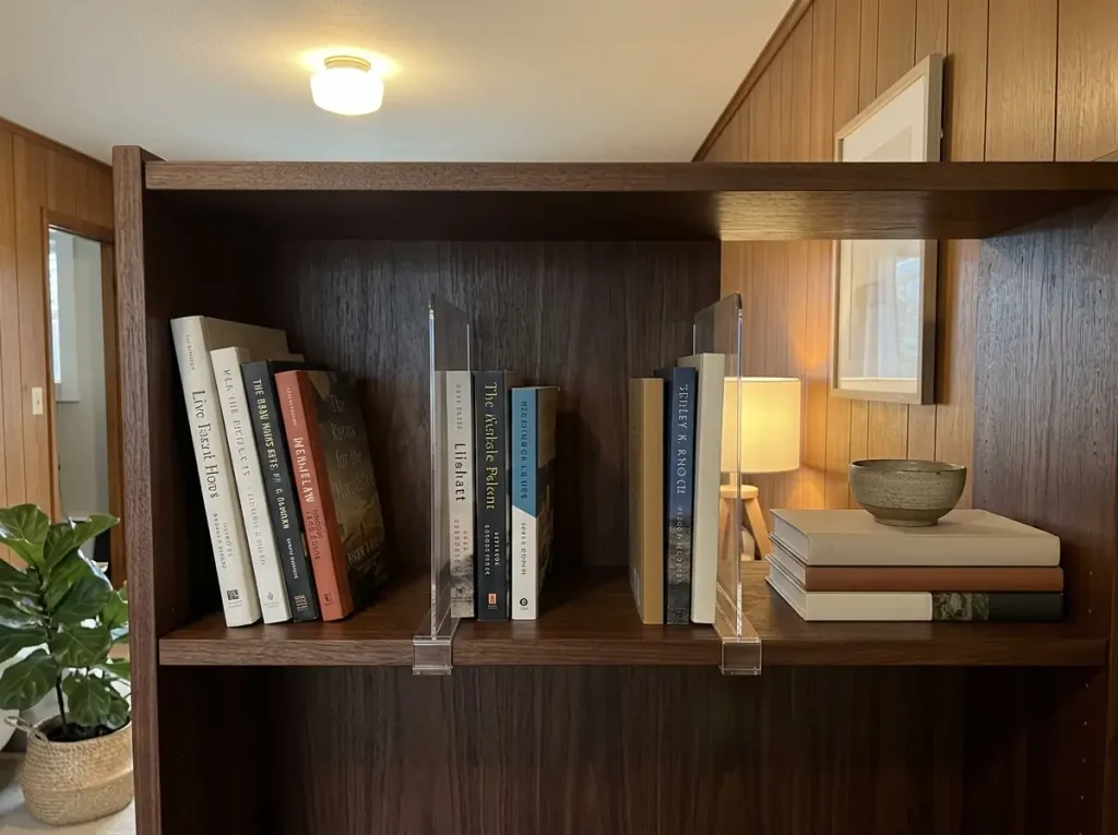 Clear acrylic shelf dividers separating book sections with breathing room on a wooden bookshelf