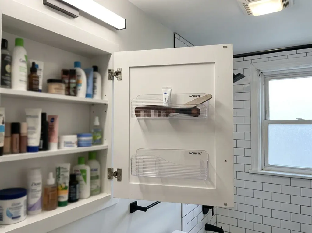 Narrow tray organizer mounted on the inside of a medicine cabinet door holding small bathroom items