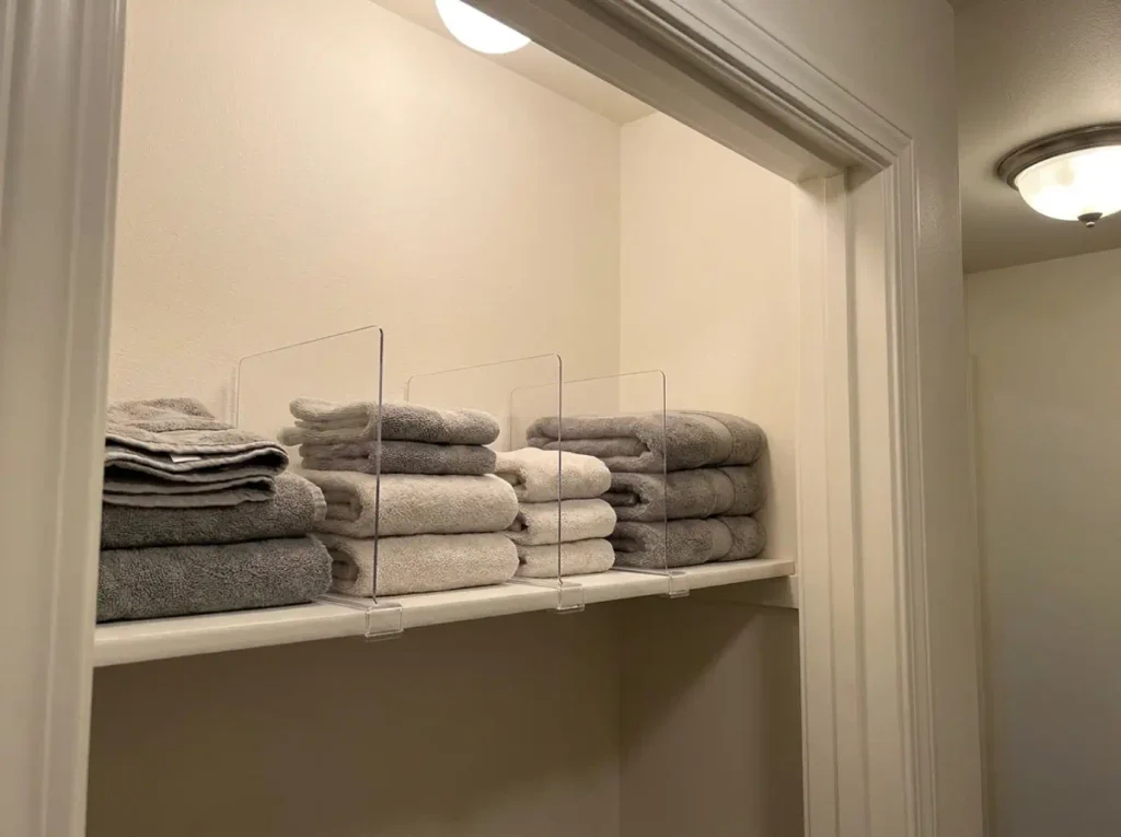 Acrylic shelf dividers holding folded towel stacks upright on a linen closet shelf