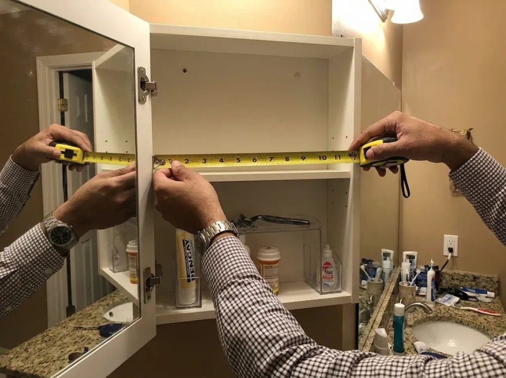 Medicine Cabinet Organization for 3-Inch Shelves 4 Hands measuring the shallow depth of a medicine cabinet shelf with a tape measure before buying organizer bins