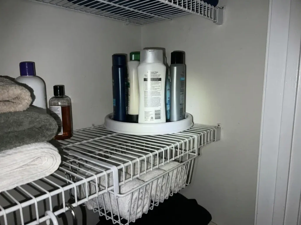 Turntable in the back corner of a deep linen closet shelf with an under-shelf basket below