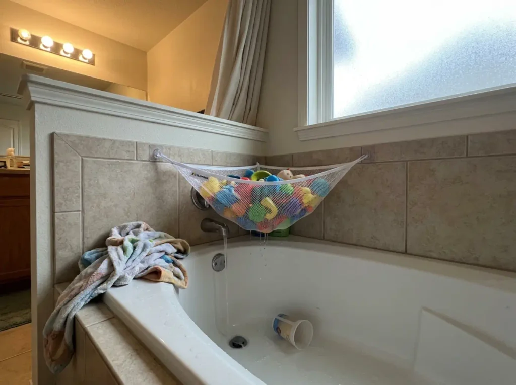 Mesh bath toy organizer mounted in a tub corner draining after a kid's bath