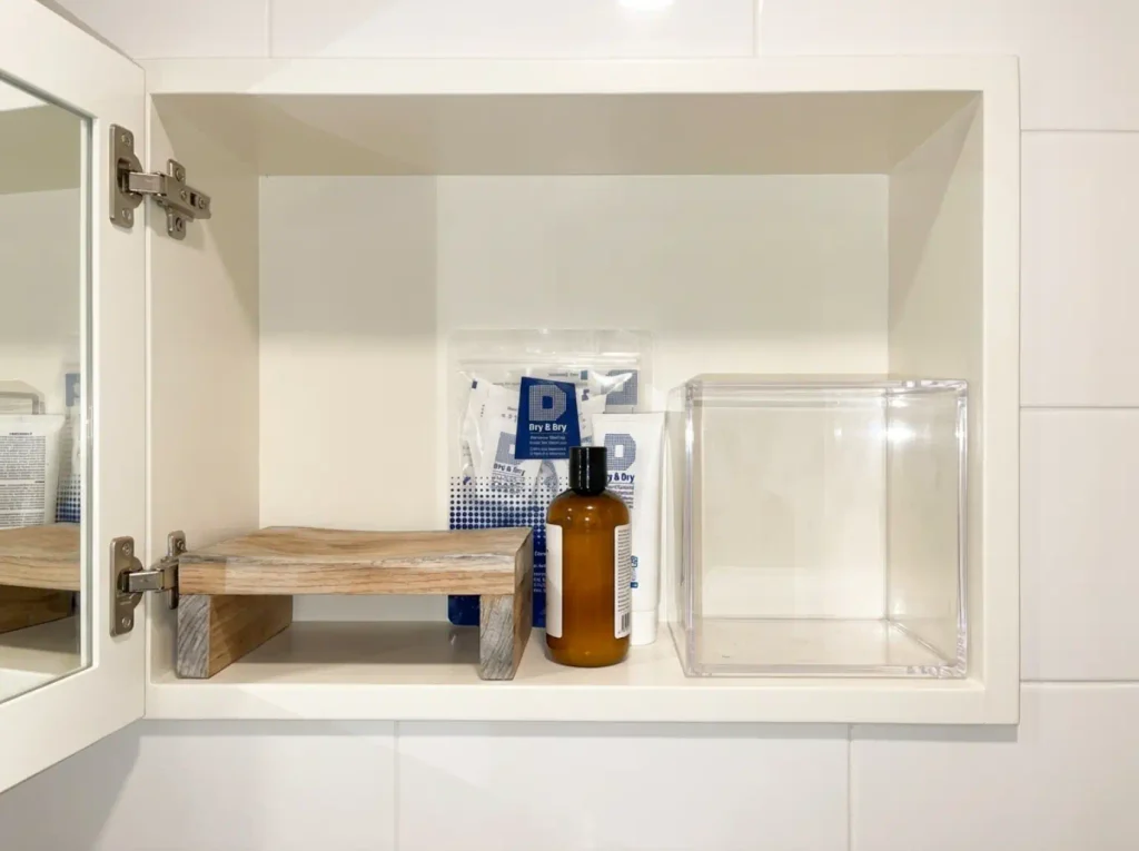 Silica gel packet tucked behind bottles on a medicine cabinet shelf beside a warped wooden organizer