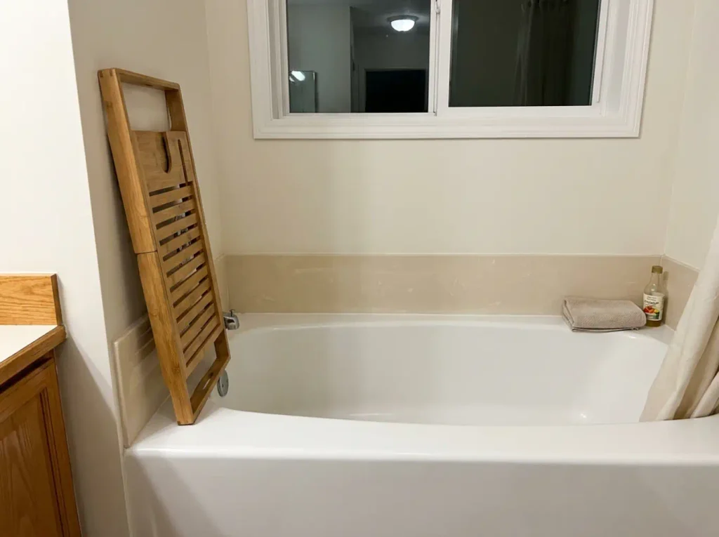 Bamboo bathtub caddy stood on end against the tub surround to dry after a bath