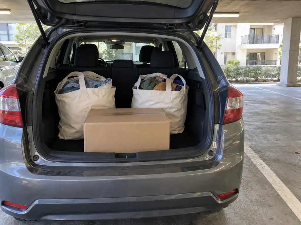 The open rear hatch of a compact car holds two canvas totes and a closed cardboard box ready for a donation drop-off