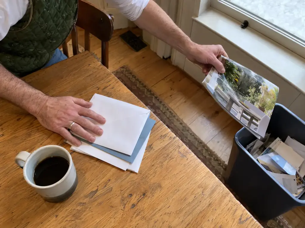 Mail Piling Up Again? A Mail Organization System That Holds 2 A man's hands lifting a glossy catalog toward a recycling bin beside a chair while three envelopes wait on the table