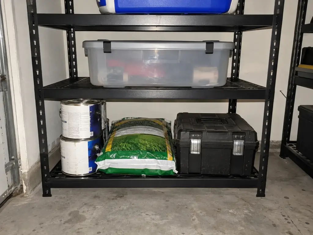 Paint cans and a boxed toolbox sit low and centered on the bottom shelf of a steel garage shelving unit