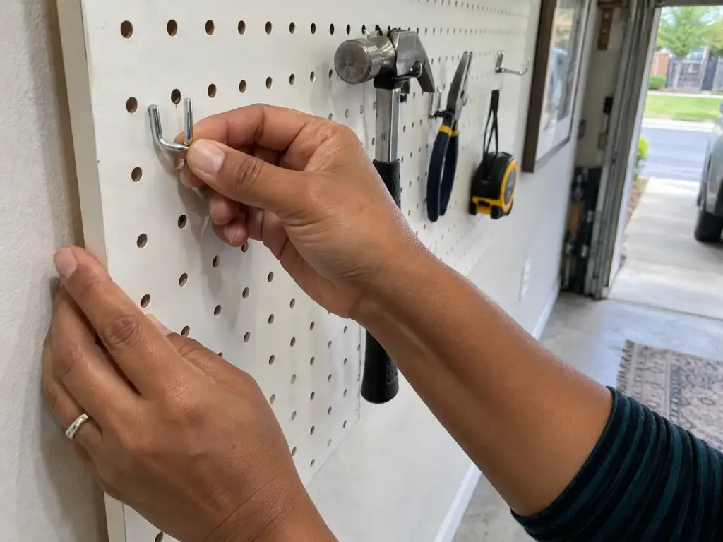 Garage Organization Ideas on a Budget, in the Right Order 3 Hand holding a metal pegboard hook against a hole on a garage pegboard to check whether the sizes match