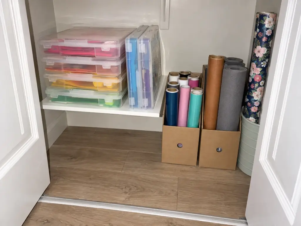 Closet interior with clear scrapbook paper cases on a shelf and rolls of vinyl and foam standing upright in rows