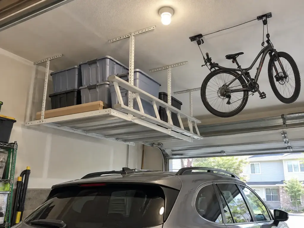 Car Still Has to Fit? Small Garage Organization Tips 7 A white overhead garage rack holds sealed bins above a parked crossover, with a bicycle raised on a ceiling hoist beside it